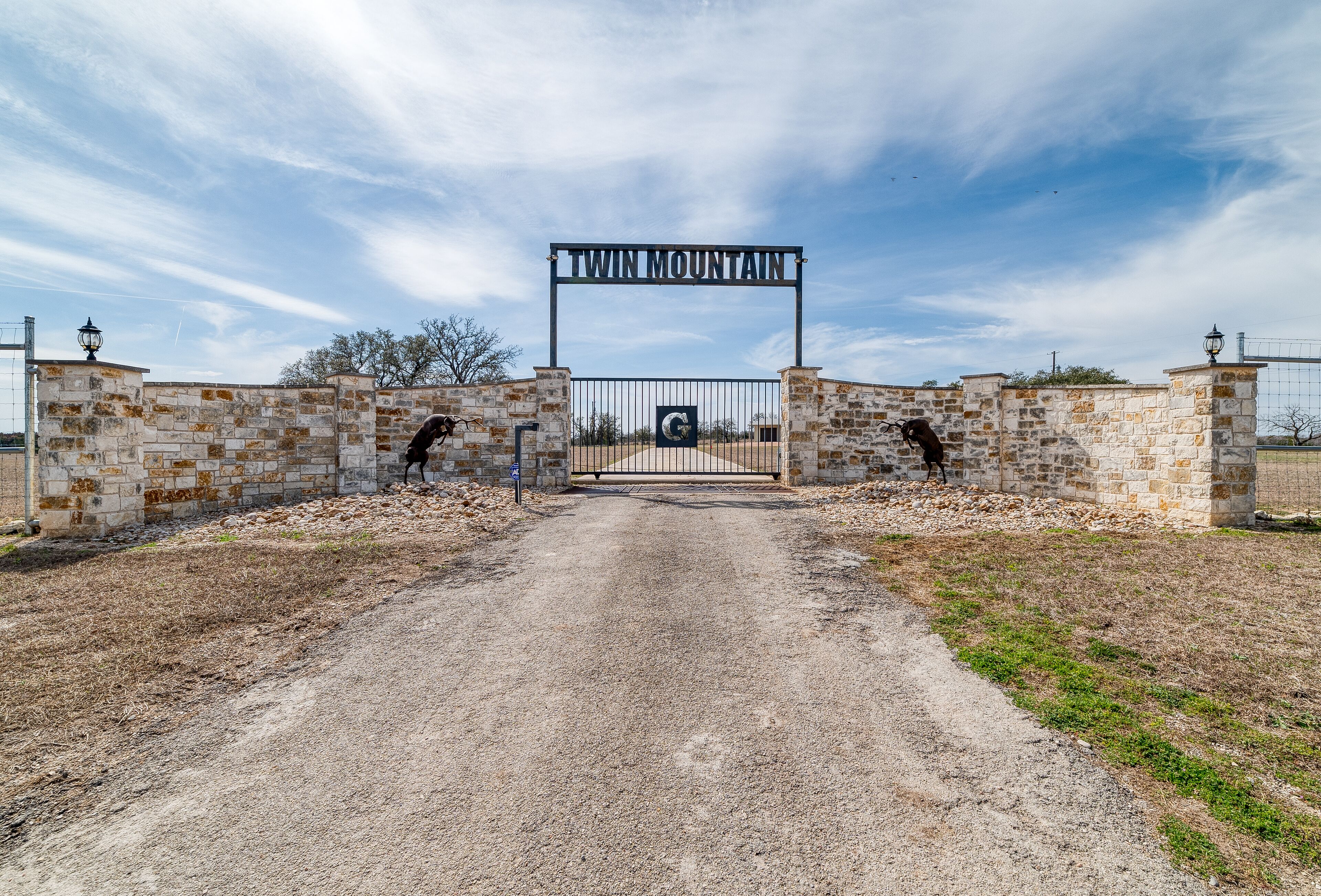 A gravel driveway leading to a gated entrance with a sign reading "Twin Mountain."