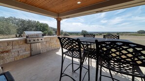 Een terras buiten met een stenen muur, een barbecue en metalen stoelen.