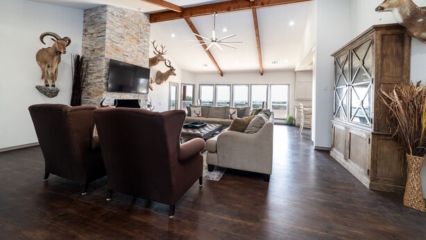 Een ruime woonkamer met donker houten vloeren, een stenen open haard en een grote televisie aan de muur. Er staan twee bruine leren fauteuils en een beige bank.