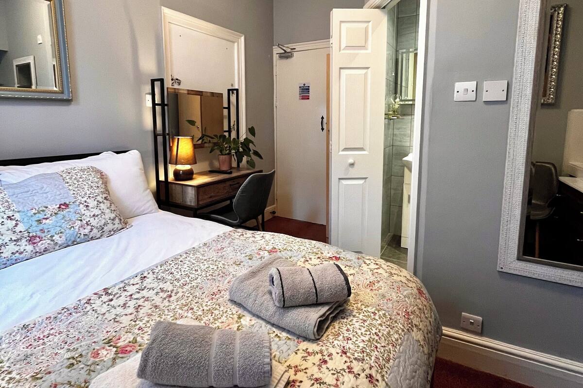 A hotel room with a bed, a desk, a chair, and a mirror.