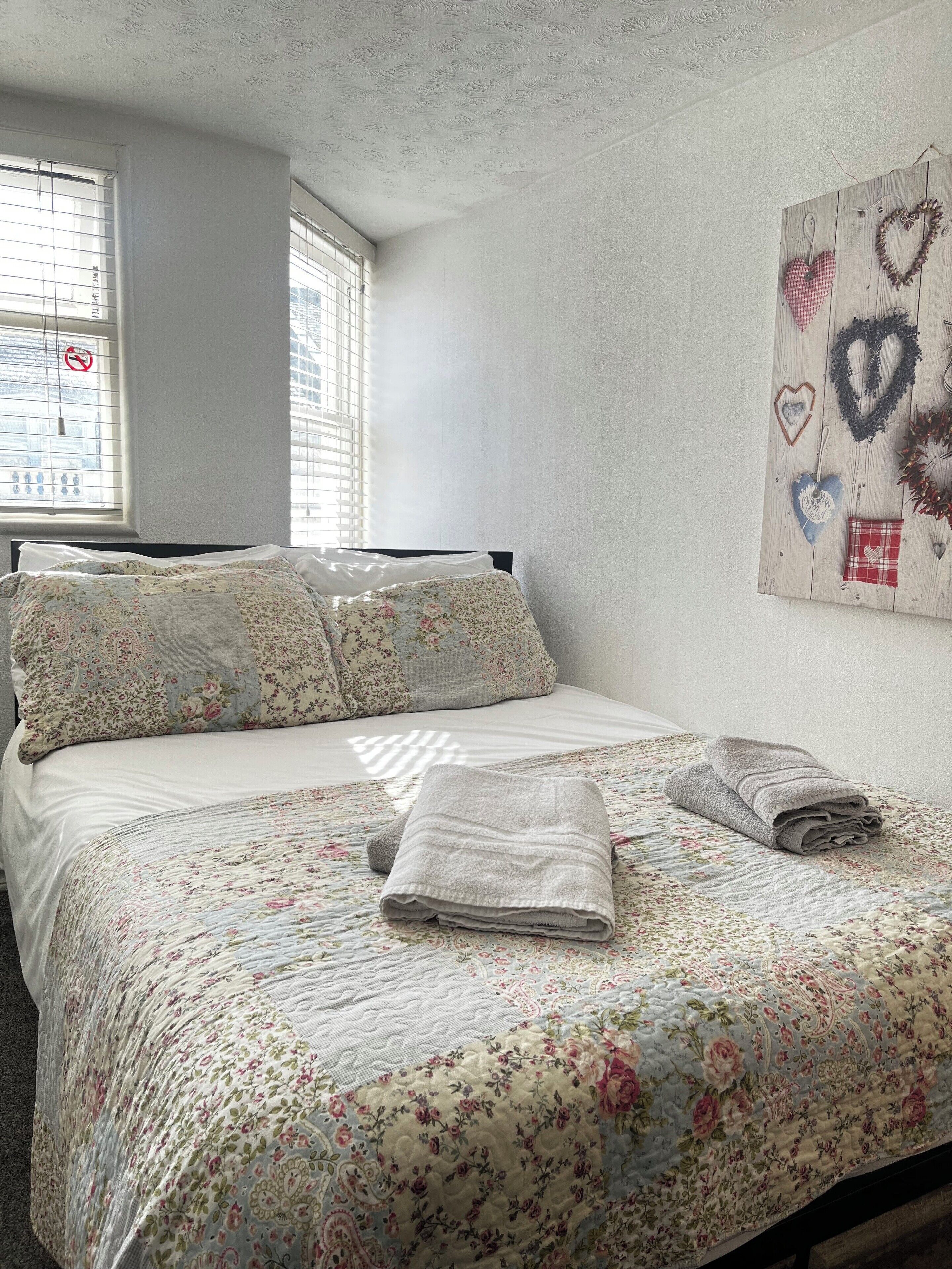 A neatly made bed with floral bedding and a heart-shaped pillow.