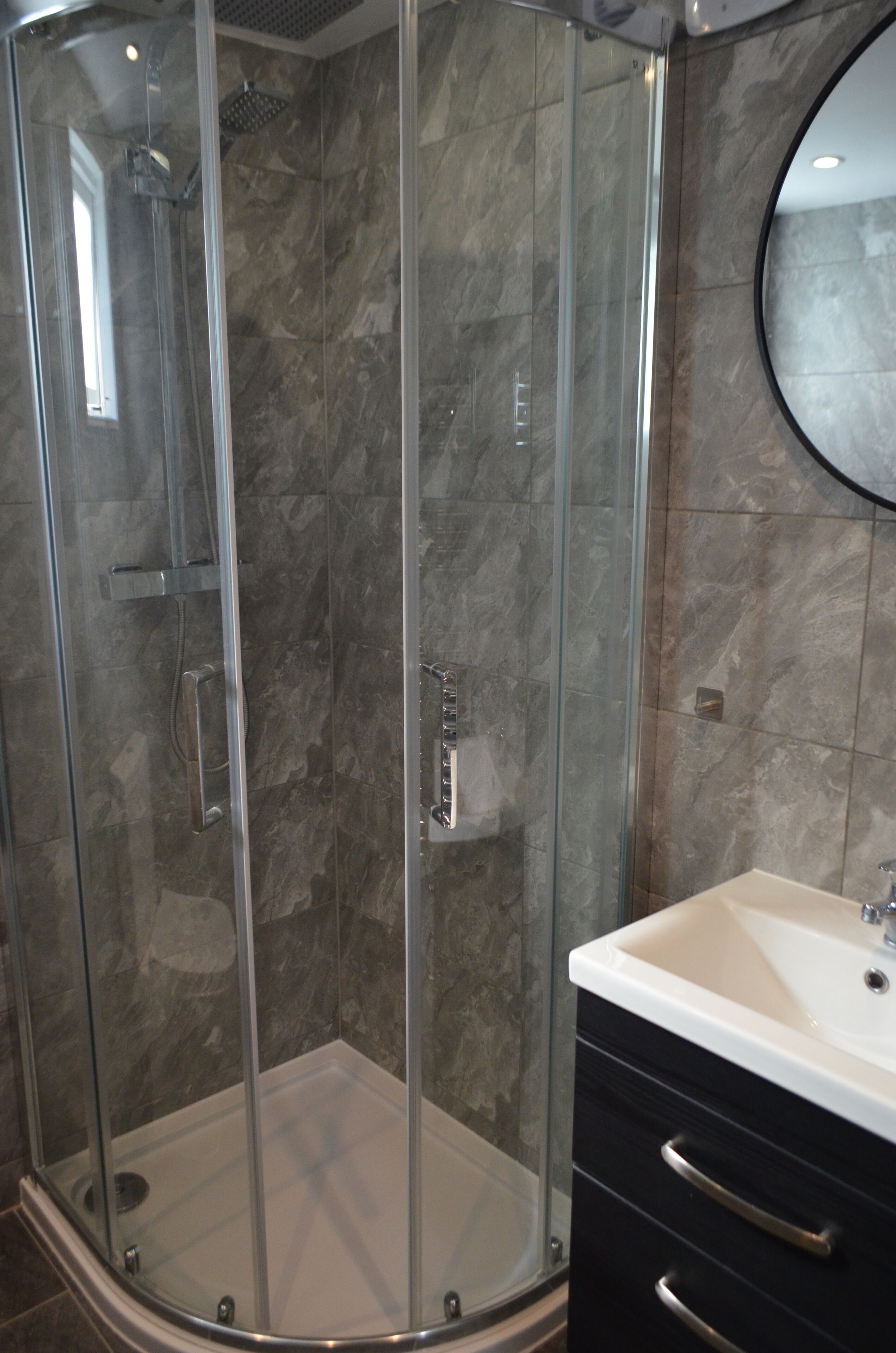 A glass-enclosed shower with a handheld showerhead, a wall-mounted faucet, and a tiled floor.