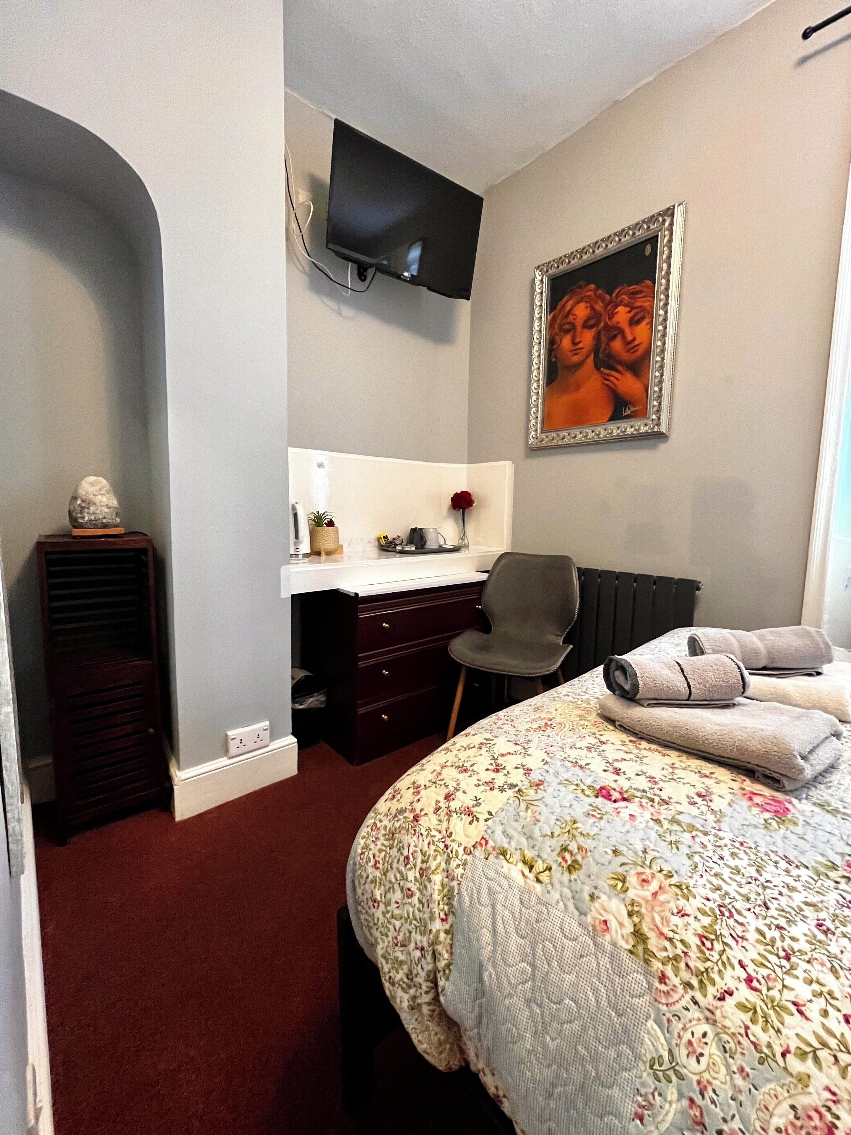 Una habitación de hotel con cama, escritorio, silla, televisor y un cuadro en la pared.