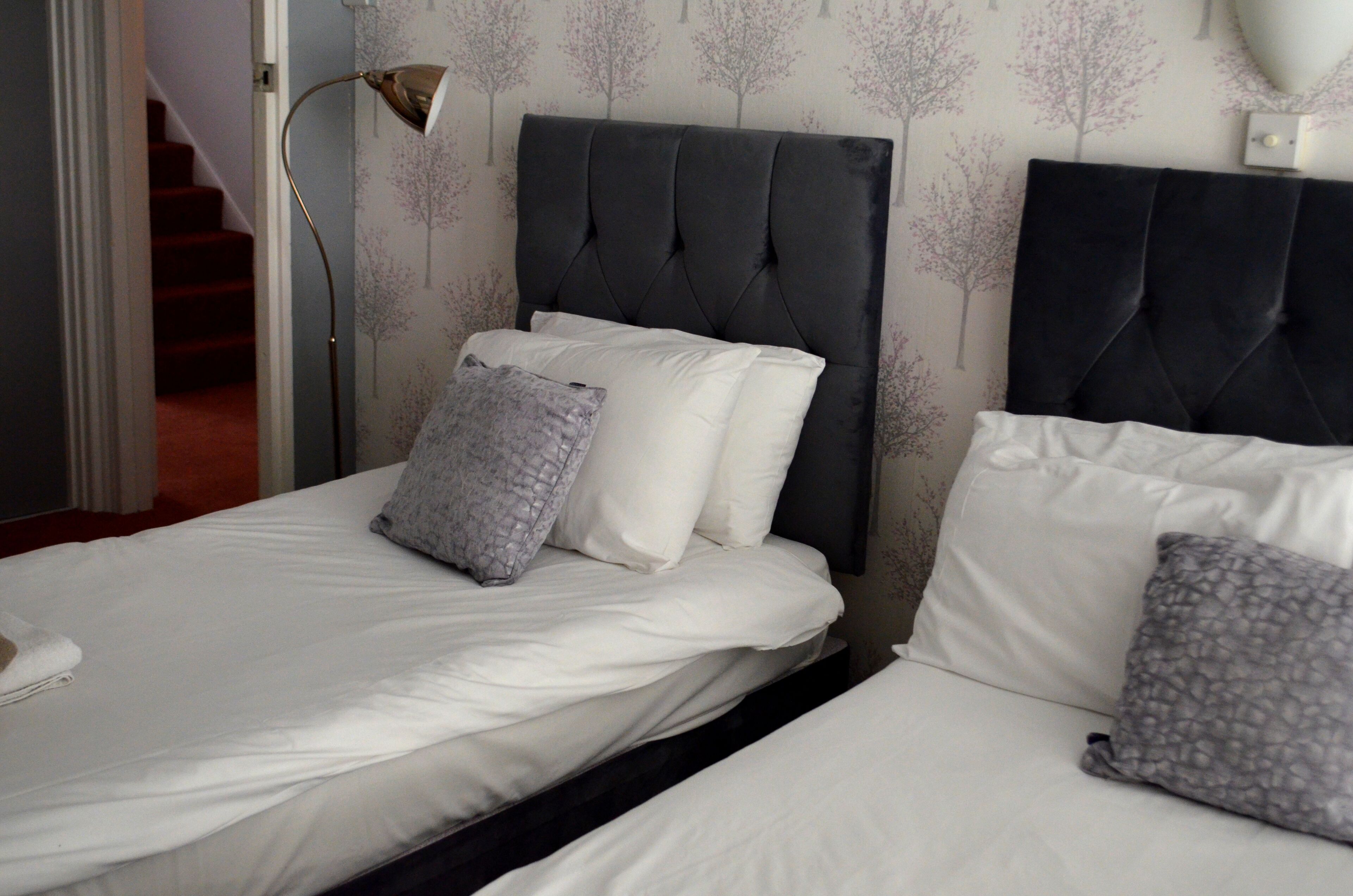 Un dormitorio con dos camas, cada una con ropa de cama blanca y almohadas grises estampadas.