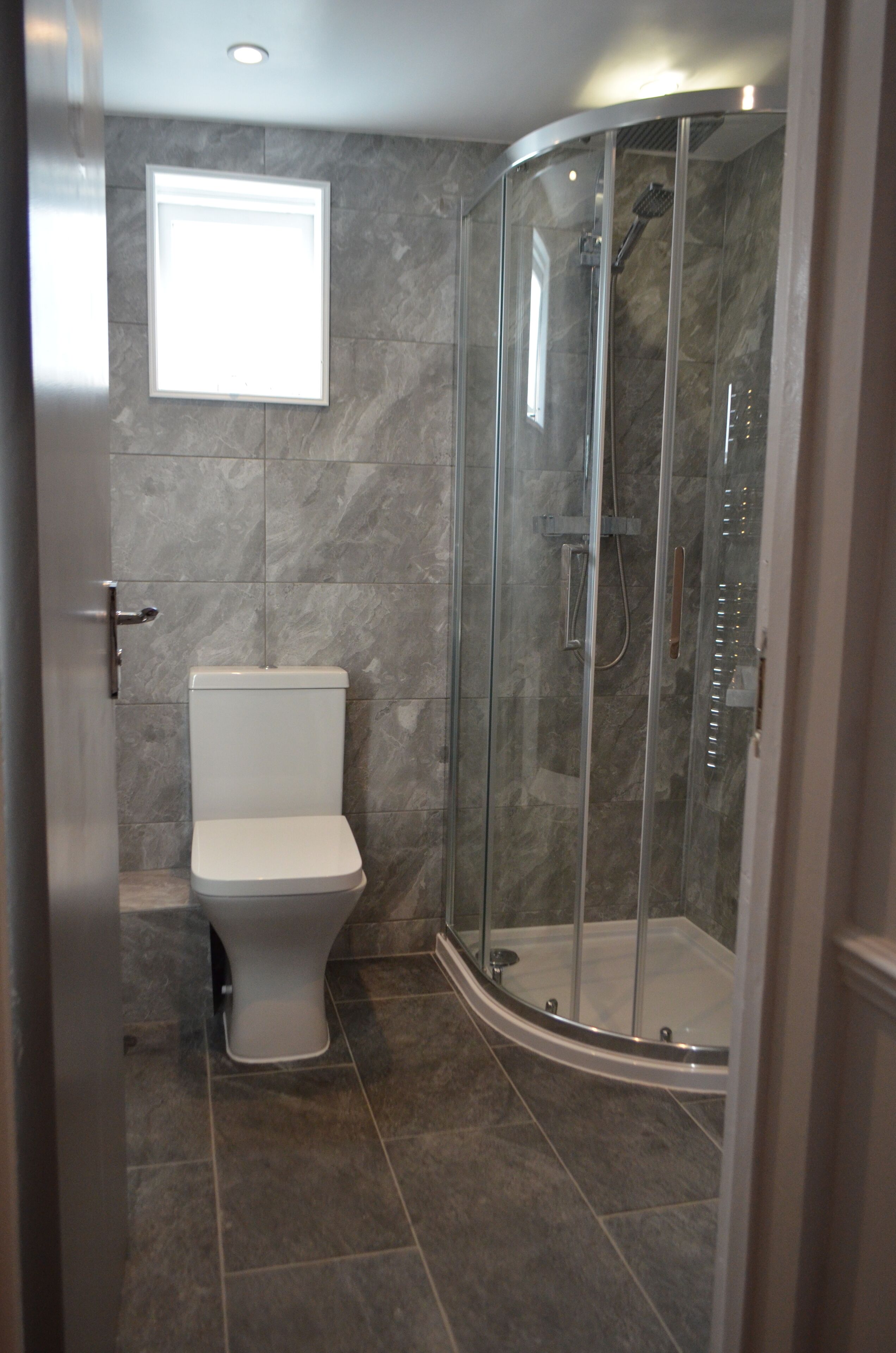 A modern bathroom with a toilet, a shower enclosure, and a window.