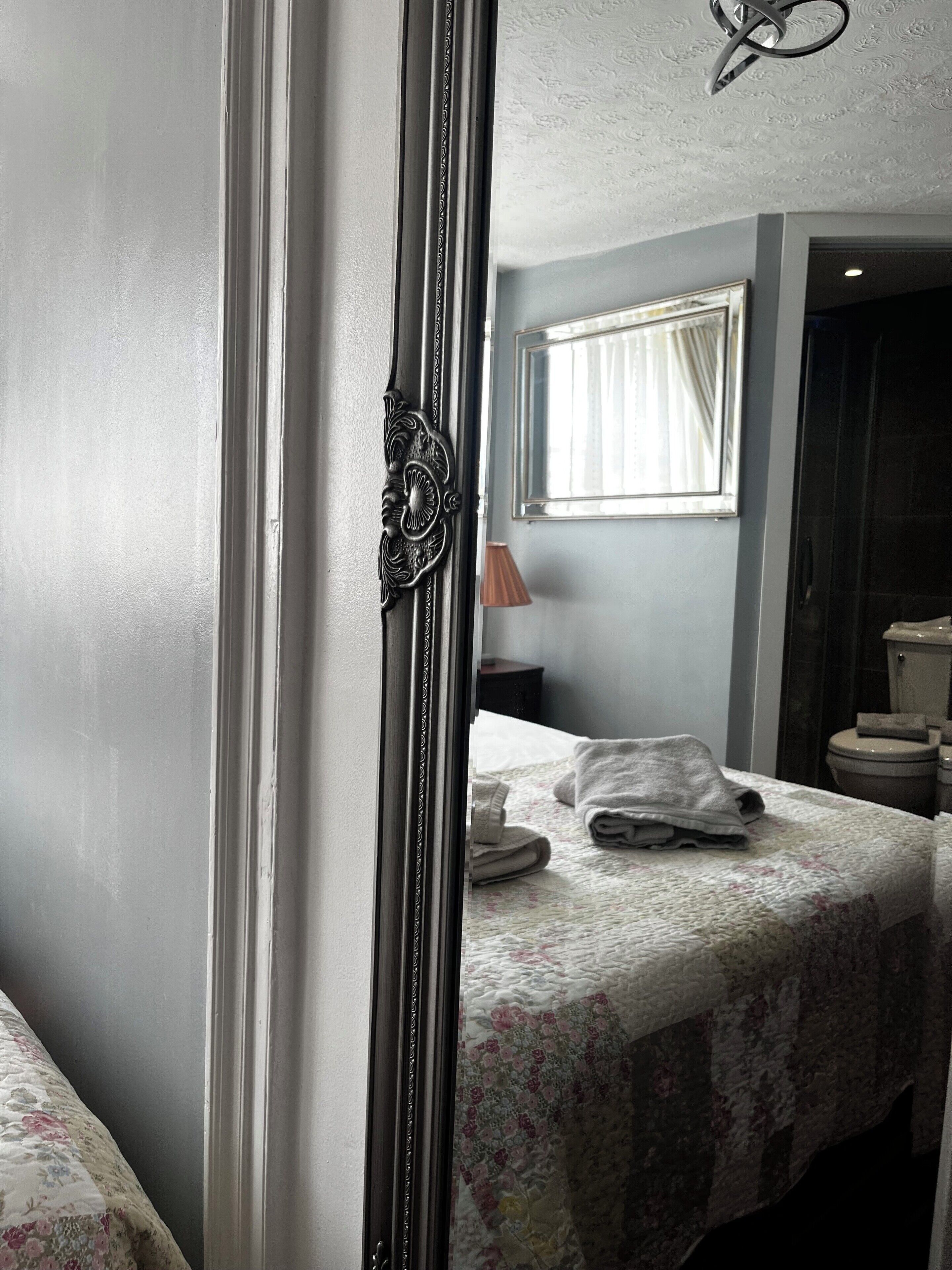 Ein Schlafzimmer mit Bett, Spiegel, Fenster und angrenzendem Badezimmer.