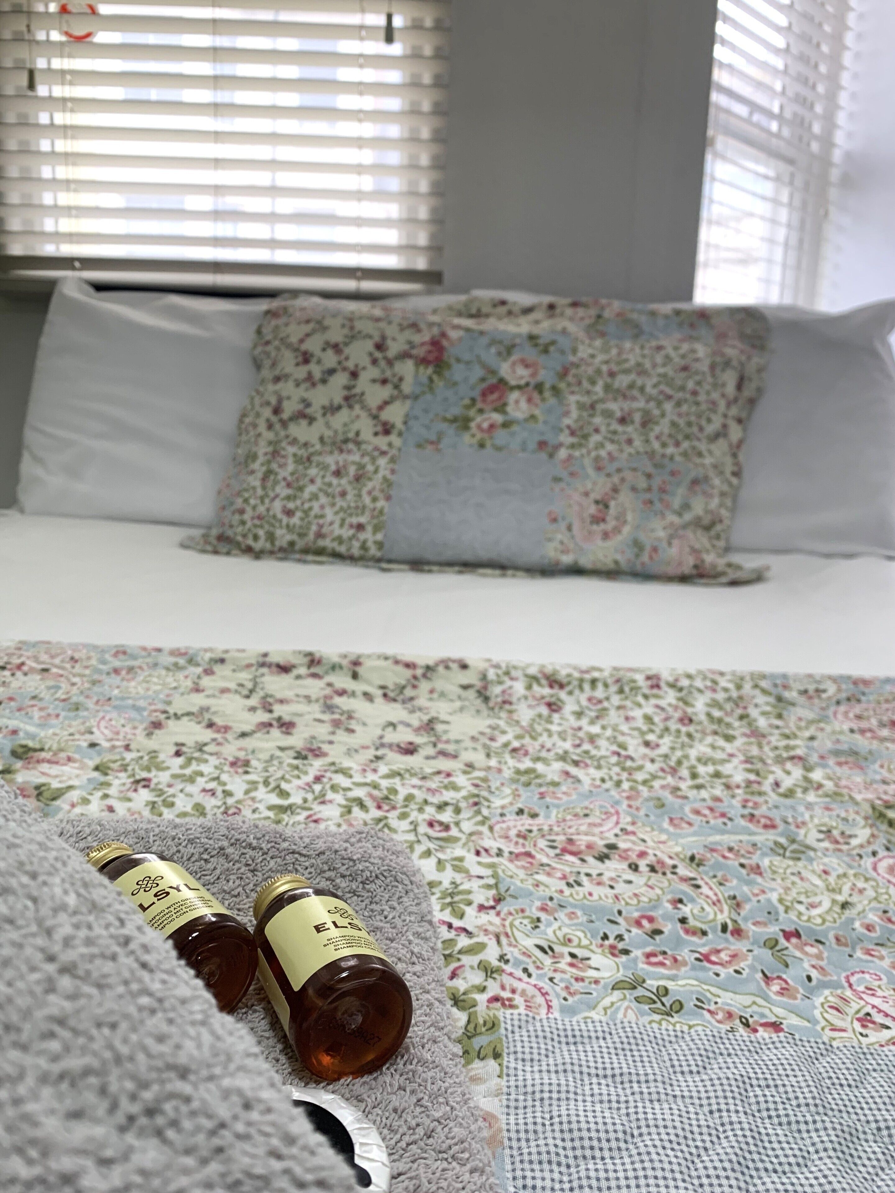 A bed with floral bedding, a grey blanket, and two bottles on a grey pillow.
