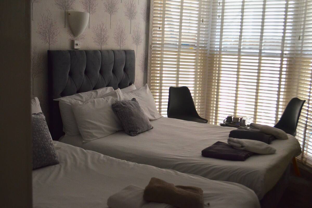 A hotel room with two beds, a large wall-mounted lamp, and a window with blinds.