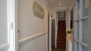 A hallway with a sign that says "Be our guest" on the wall, a staircase leading to another room, and a vase with flowers on a shelf. - Relax Inn Guest House (Brighton)