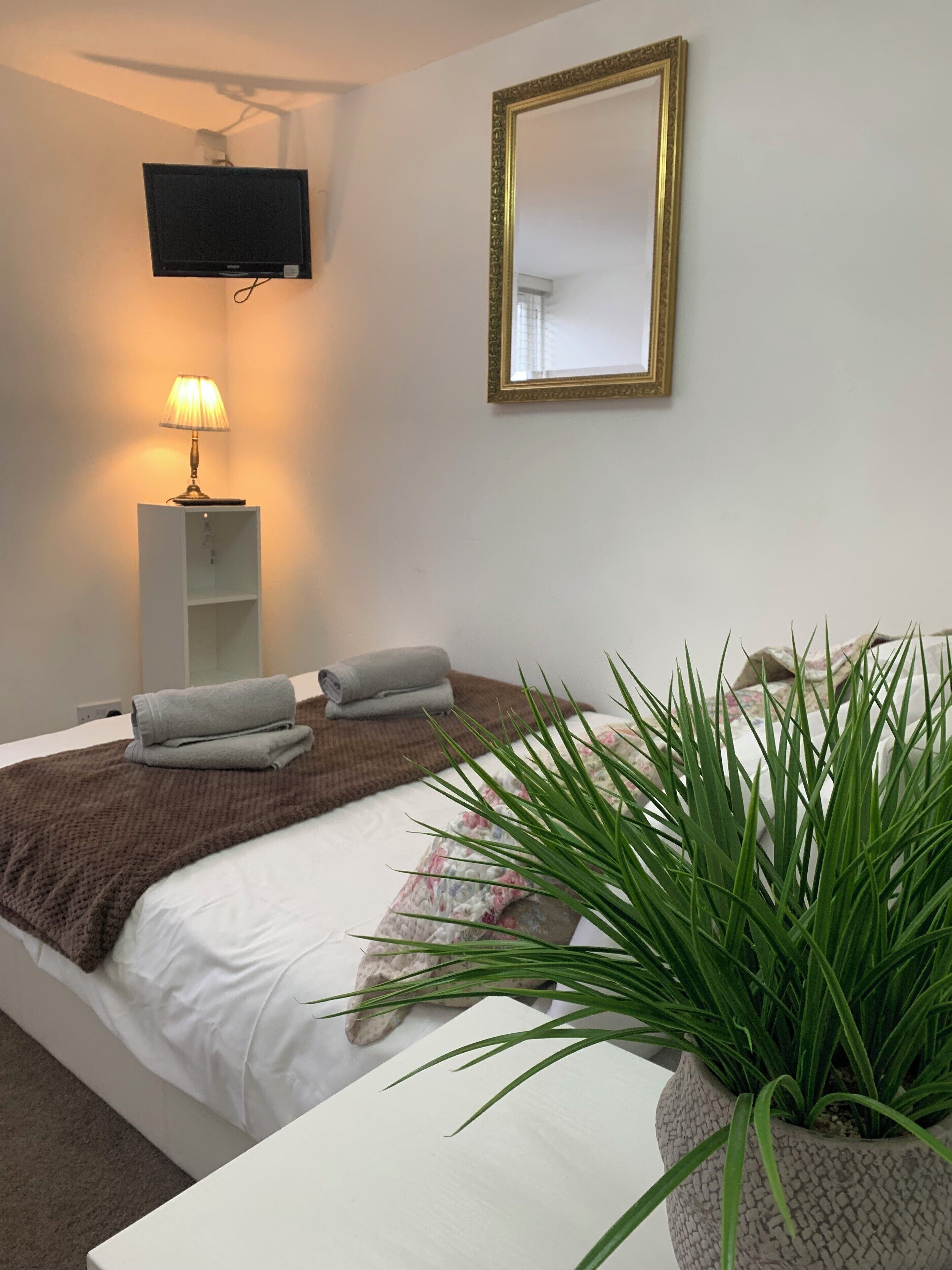 A neatly arranged bedroom with a bed, a bedside lamp, a television mounted on the wall, and a large mirror.