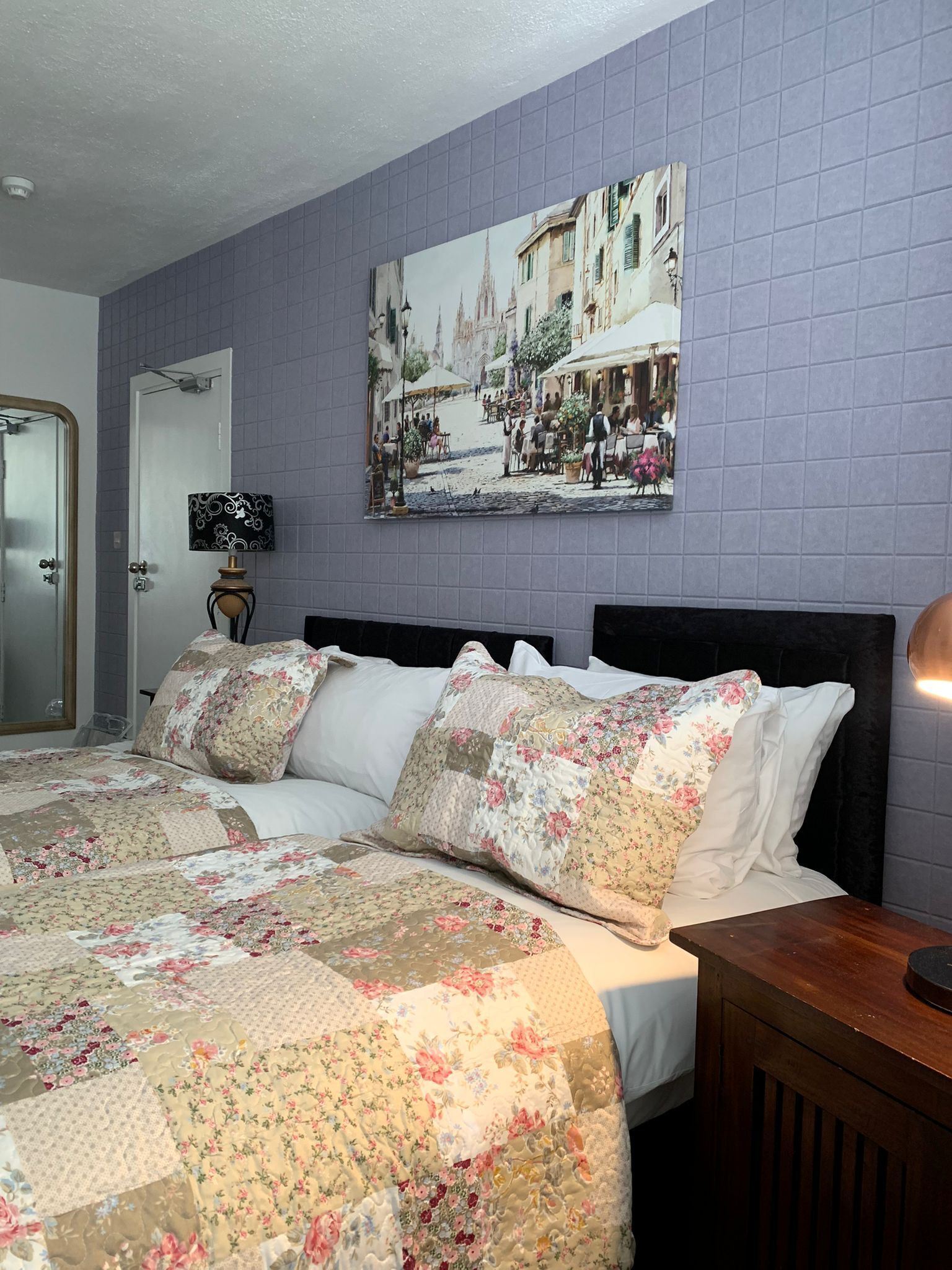 A bedroom with a bed, floral bedding, a wall-mounted painting, and a door.