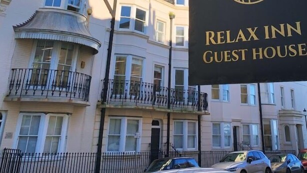 A sign for the Relax Inn Guest House with a circular logo and the name in gold lettering. - Relax Inn Guest House (Brighton)