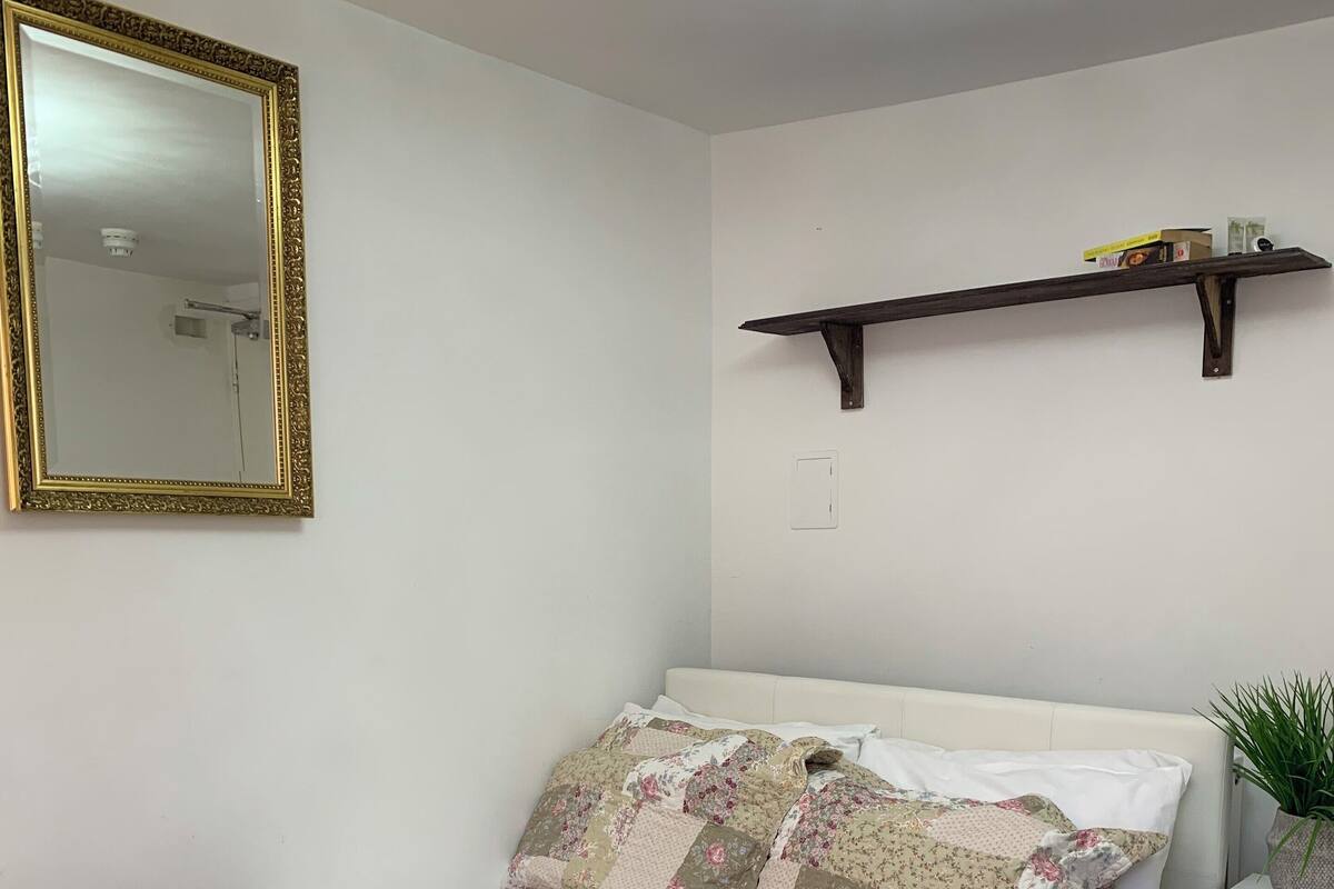 A neatly made bed with a brown blanket and two rolled towels, a white headboard, and a floral-patterned pillow.