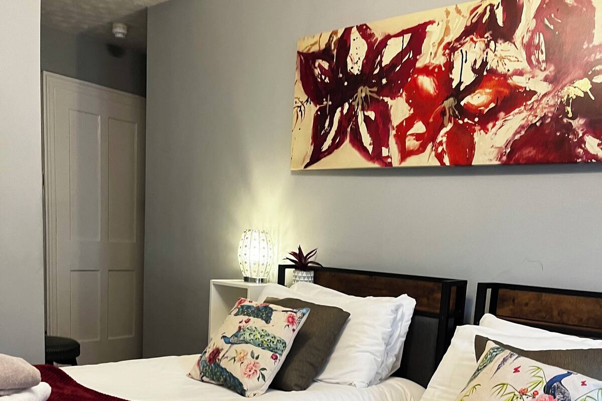 A hotel room with two beds, each with white linens and decorative pillows, a red blanket, and a wall-mounted artwork.