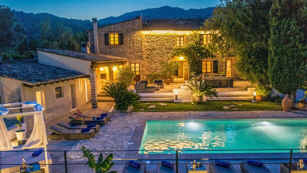 A stone house with a swimming pool, outdoor seating, and a well-lit patio area.