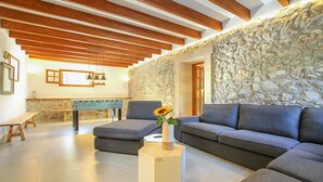 A modern living room with a stone wall, wooden beams, a sofa, a coffee table, and a foosball table.