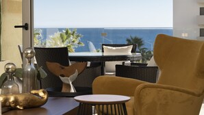 A room with a view of the ocean, a wicker table, a yellow armchair, and decorative items.