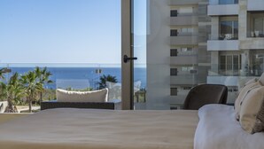A hotel room with a large bed, a view of the ocean, and a balcony with a wicker chair.