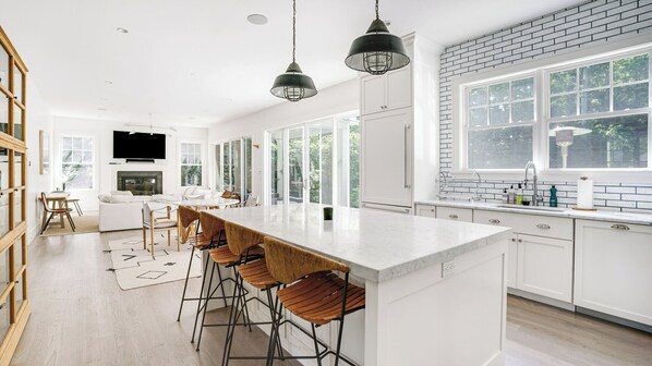 A modern kitchen with a large island, bar stools, and a brick accent wall.