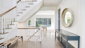A spacious hallway with a wooden staircase, a bench, and a large mirror on the wall.