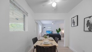 Un comedor con una mesa dispuesta para cuatro, un ventilador de techo y vistas a una sala de estar con un sofá y un televisor.