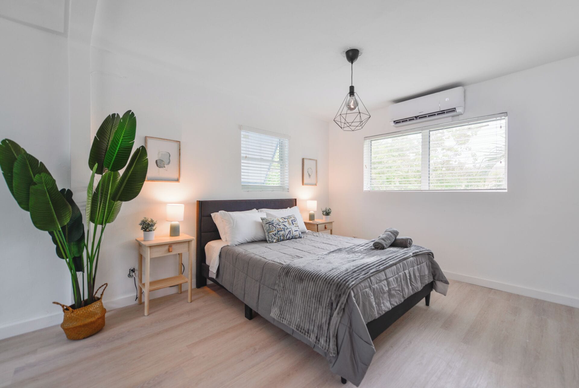 Un dormitorio con cama, mesitas de noche, una planta en maceta y una ventana con persianas.