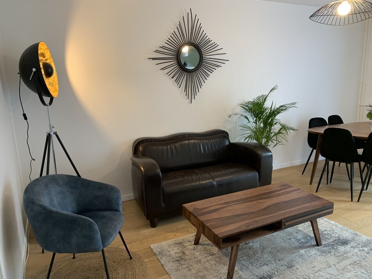 Una sala de estar moderna con un sofá de cuero, un sillón azul, una mesa de centro de madera, una lámpara de pie y un comedor con mesa y sillas.