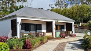 A two-story house with a garage, surrounded by a garden with various plants and flowers. - Les Chambres et table d'hôte du Voyageur/ chambre citronnelle (La Plaine Des Palmistes)