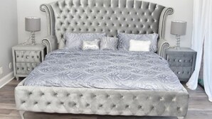 Une chambre à coucher avec une tête de lit capitonnée, une couvre-lit à motifs et deux tables de chevet avec des lampes.