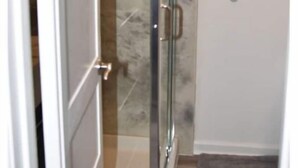 Une cabine de douche fermée par des parois de verre, avec un mur en marbre et une porte blanche.