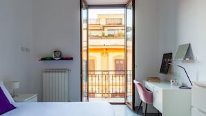 A modern bedroom with a bed, a desk, and a chair. There is a view of a balcony with a railing and buildings in the background. - Ferdinando Art House by Wonderful Italy (Naples)