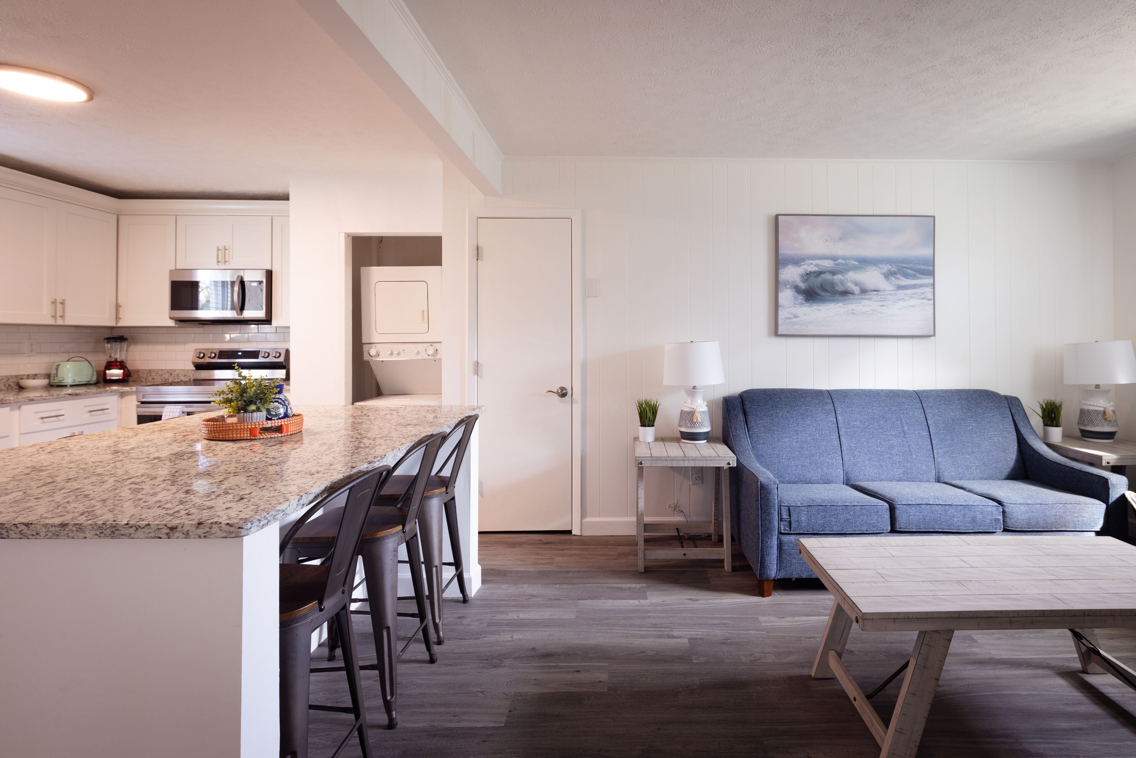 A modern kitchen with granite countertops, stainless steel appliances, and a dining area with a blue sofa and a wooden coffee table.