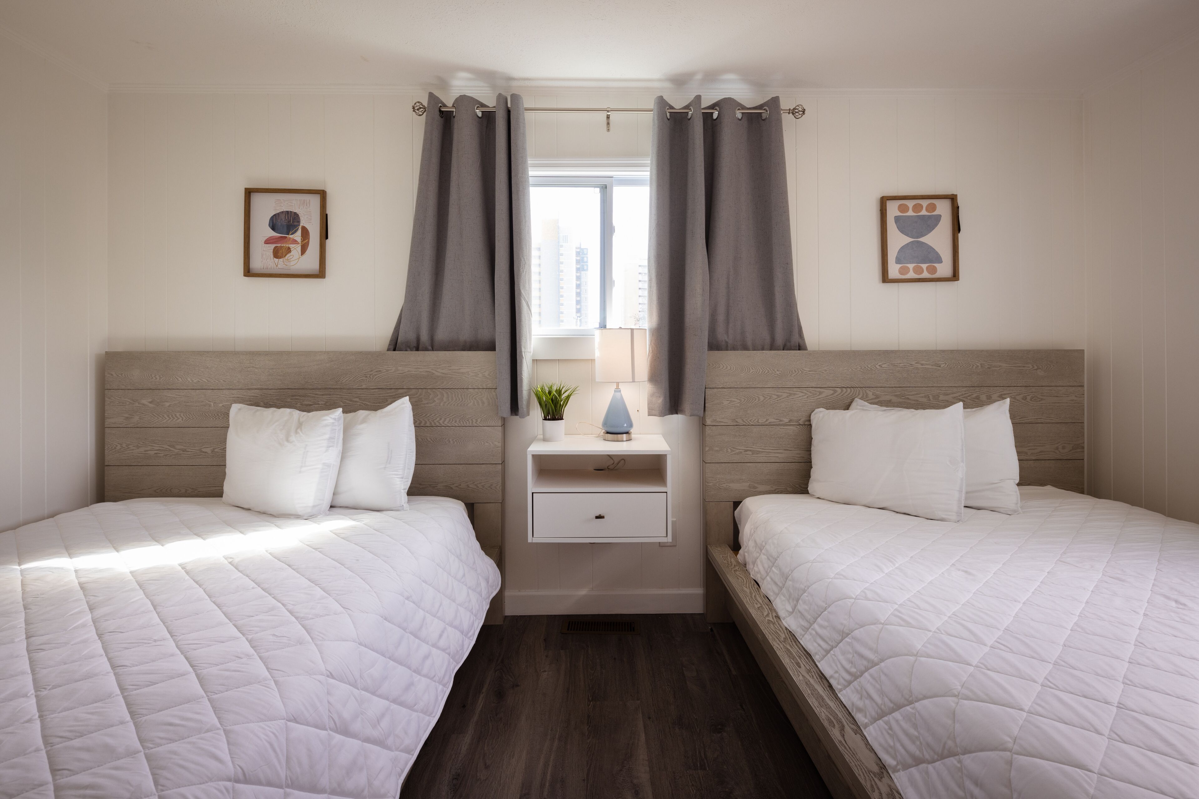 Een tweeepersoonskamer met twee bedden, een nachtkastje met een lamp en een raam met gordijnen.