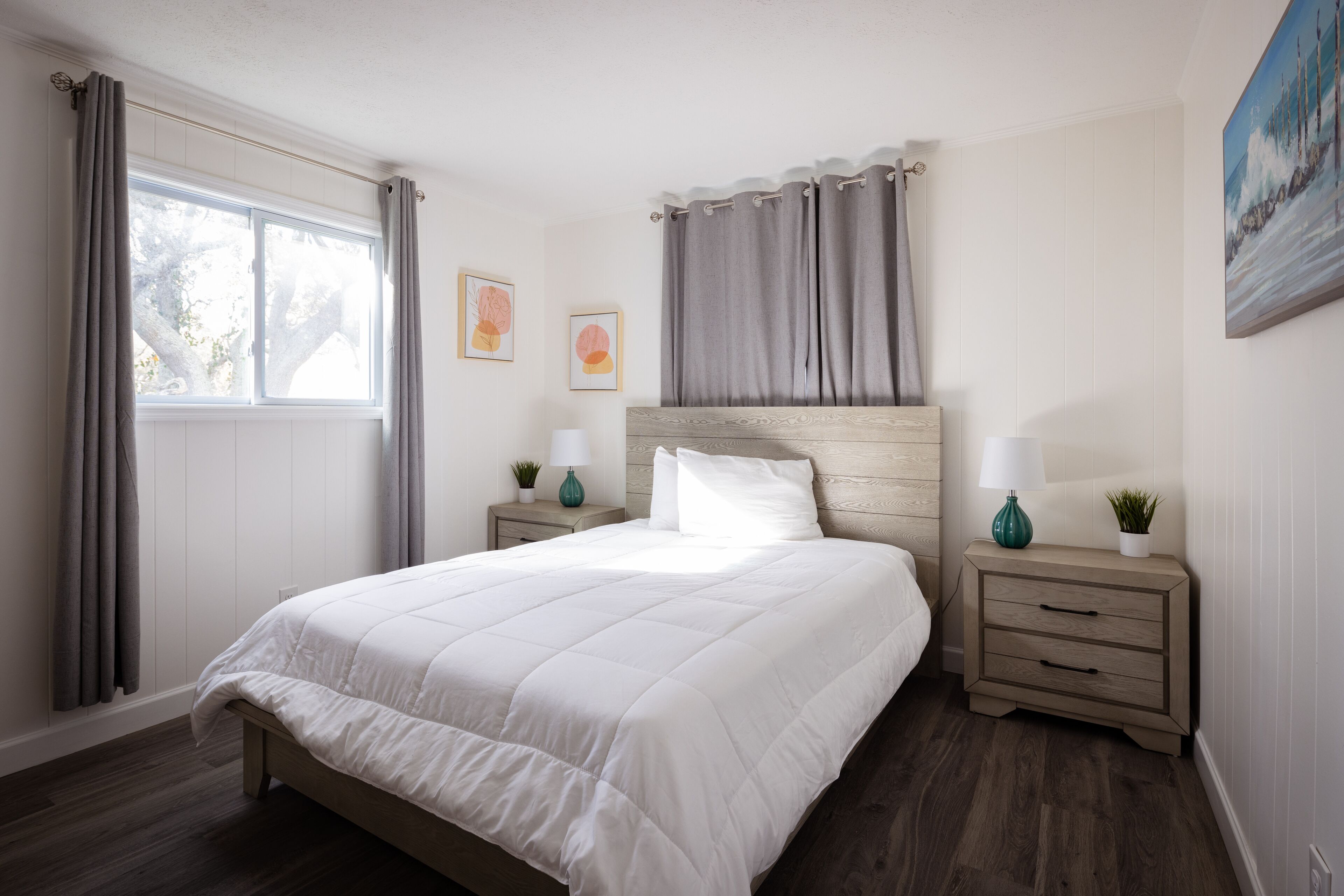Une chambre à coucher avec un grand lit, deux tables de chevet, une tête de lit et une fenêtre avec des rideaux.