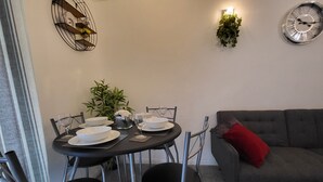 A dining area with a round table set for four, surrounded by chairs, a grey sofa with a red pillow, and a wall-mounted clock. - Captivating 2-bed Apartment in Southend-on-sea (Southend-on-Sea)