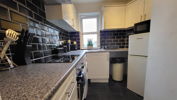A kitchen with black and white tiles, a stove, a microwave, and a dishwasher. - Captivating 2-bed Apartment in Southend-on-sea (Southend-on-Sea)
