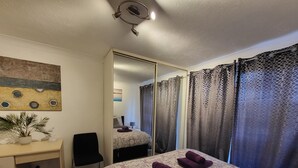 A hotel room with a bed, a desk, a chair, a mirror, and a window with curtains. - Captivating 2-bed Apartment in Southend-on-sea (Southend-on-Sea)