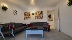 A living room with a grey sofa, a white coffee table, and a wall clock. There are two patterned wall hangings and a plant on the wall. - Captivating 2-bed Apartment in Southend-on-sea (Southend-on-Sea)
