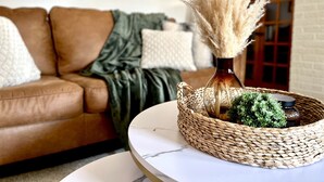 A living room with a brown leather sofa, a round white table, and a woven basket containing pampas grass and a small plant. - Peaceful & Clean Getaway/3BR-By KWU & DnTown (Salina)