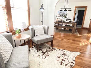 A cozy living room with a gray armchair, a white couch, a wooden dining table, and a cowhide rug.