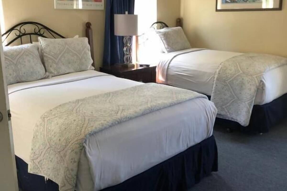 Habitación de hotel con dos camas, una mesita de noche, una lámpara y dos cuadros en las paredes.