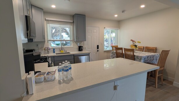 A modern kitchen with a central island, a dining area with wooden chairs, and a small table with a floral tablecloth. - Rest Haven Motel (Santa Monica)