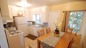 A compact kitchen with a stove, refrigerator, and dining table with chairs. - Rest Haven Motel (Santa Monica)