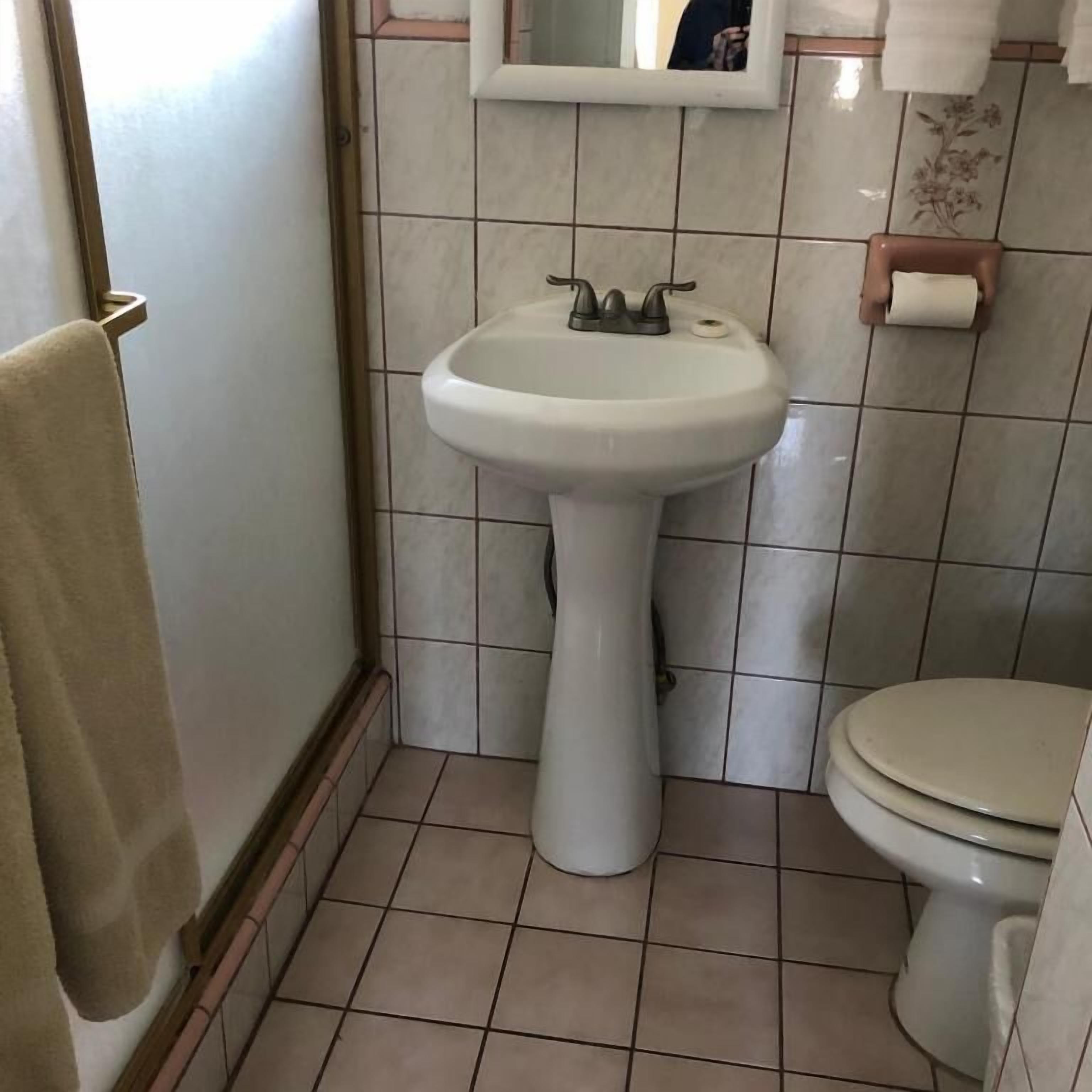 Pieni kylpyhuone, jossa on jalkapallipylväsallas, wc ja peili altaan yläpuolella.