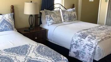 Dos camas con ropa de cama azul y blanca a cuadros, una mesita de noche con lámpara y un cuadro en la pared.