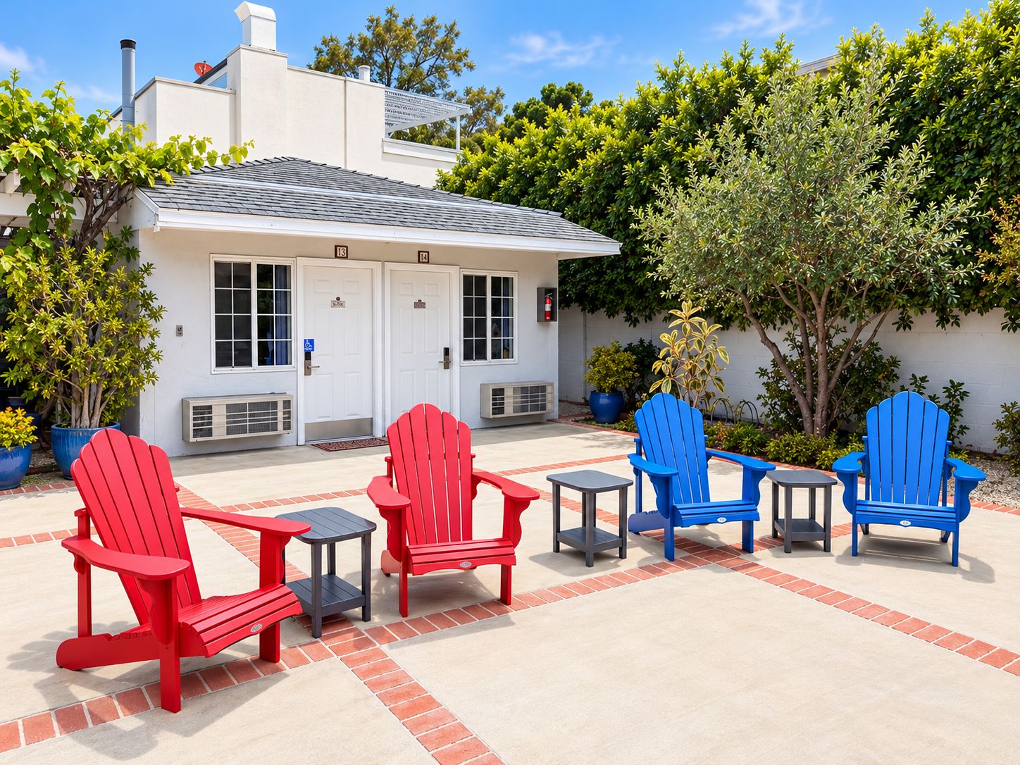 A building with a white exterior, multiple doors, and a covered patio area with red and blue Adirondack chairs and small tables.