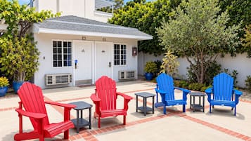 A building with a white exterior, multiple doors, and a covered patio area with red and blue Adirondack chairs and small tables.