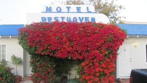A motel sign with red flowers in front. - Rest Haven Motel (Santa Monica)