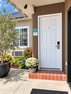 A hotel entrance with a white door marked with the number 1, a sign indicating rooms 2-9, and a potted plant with white flowers. - Rest Haven Motel (Santa Monica)