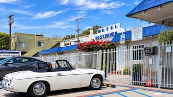 Un descapotable blanco estacionado frente a un motel con techo azul y un letrero que dice 'Motel Resthaven'.